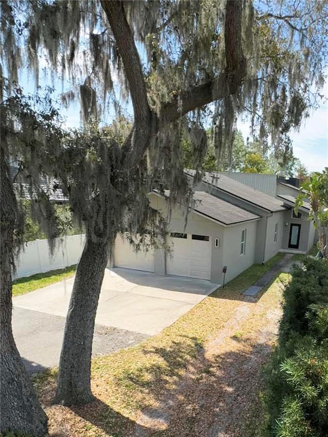 view of side of home featuring a garage, fence, concrete driveway, and stucco siding