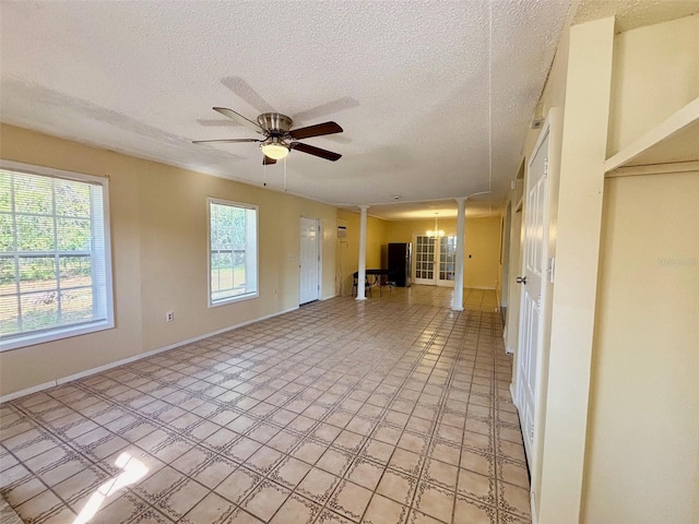 unfurnished living room featuring ceiling fan with notable chandelier, a textured ceiling, baseboards, and decorative columns