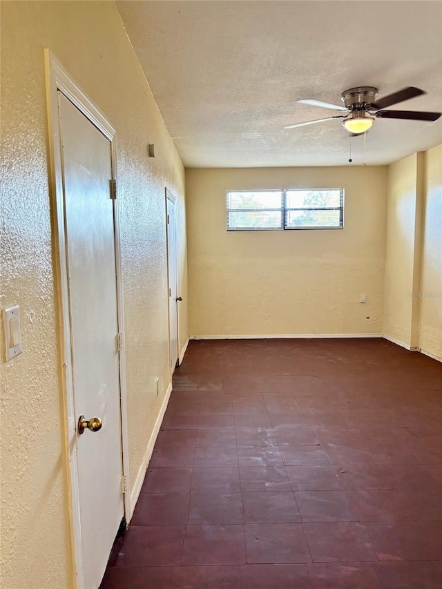 spare room featuring baseboards, a textured ceiling, ceiling fan, and a textured wall