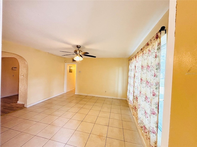 spare room with light tile patterned floors, baseboards, arched walkways, and a ceiling fan