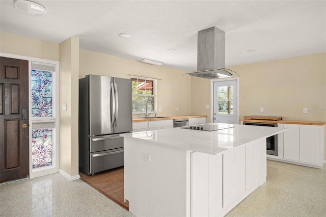 kitchen with island range hood, white cabinets, freestanding refrigerator, light speckled floor, and a sink