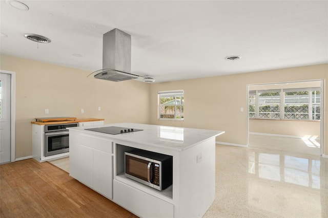 kitchen with a center island, island exhaust hood, stainless steel appliances, visible vents, and white cabinetry