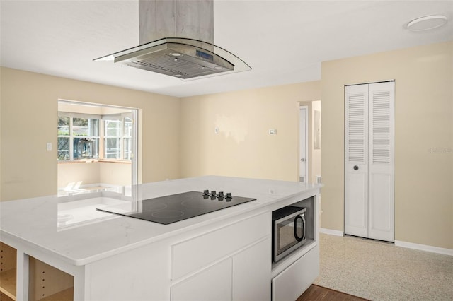 kitchen featuring light countertops, stainless steel microwave, white cabinets, baseboards, and black electric cooktop