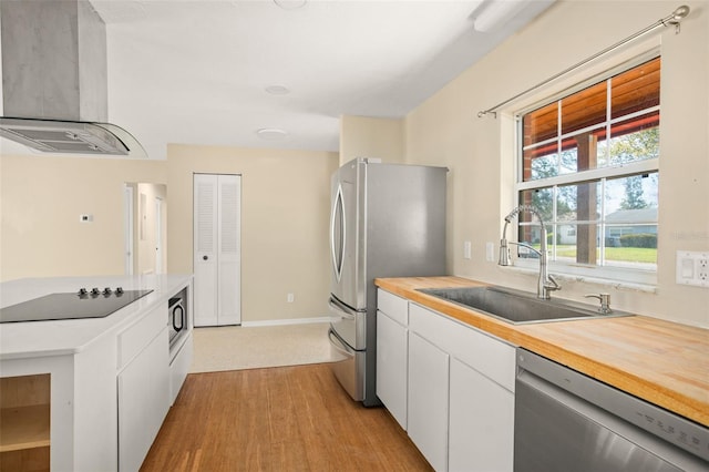 kitchen with stainless steel appliances, a sink, white cabinets, wooden counters, and wall chimney exhaust hood