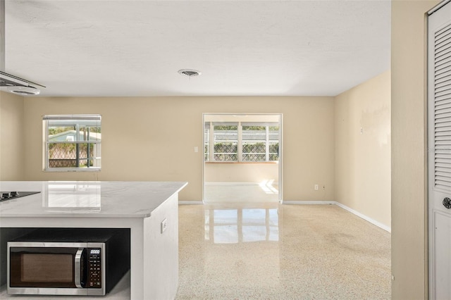 kitchen featuring baseboards, visible vents, stainless steel microwave, open floor plan, and speckled floor