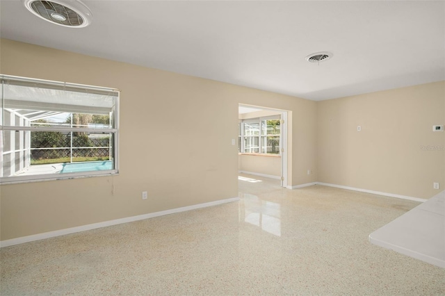 empty room with visible vents, baseboards, and speckled floor