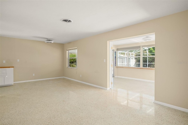 empty room featuring speckled floor, visible vents, and baseboards