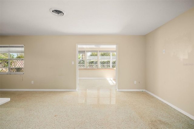 empty room with speckled floor, visible vents, and baseboards