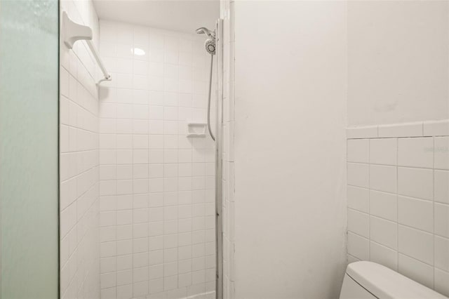 full bath with toilet, a stall shower, and tile walls