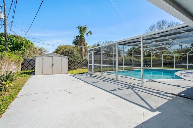 view of pool featuring glass enclosure, a fenced backyard, an outbuilding, a storage unit, and a patio area