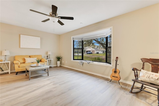 living area featuring baseboards, ceiling fan, and light wood finished floors