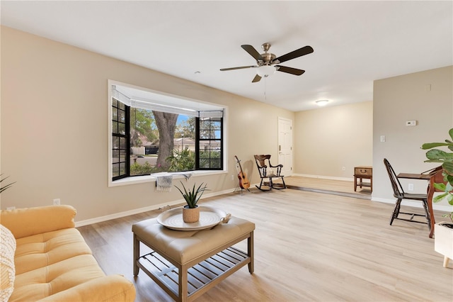 living area with a ceiling fan, light wood-style flooring, and baseboards