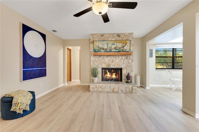 unfurnished living room featuring baseboards, visible vents, ceiling fan, wood finished floors, and a stone fireplace