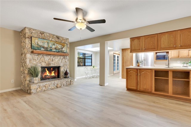 unfurnished living room with a ceiling fan, a fireplace, light wood-style flooring, and baseboards