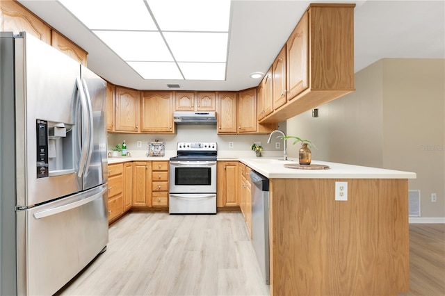 kitchen with light wood-style flooring, appliances with stainless steel finishes, light countertops, under cabinet range hood, and a sink