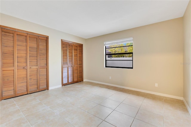 unfurnished bedroom with multiple closets, baseboards, and light tile patterned floors