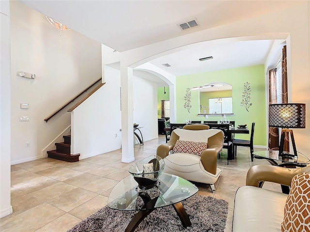 living room featuring arched walkways, visible vents, stairway, light tile patterned flooring, and baseboards