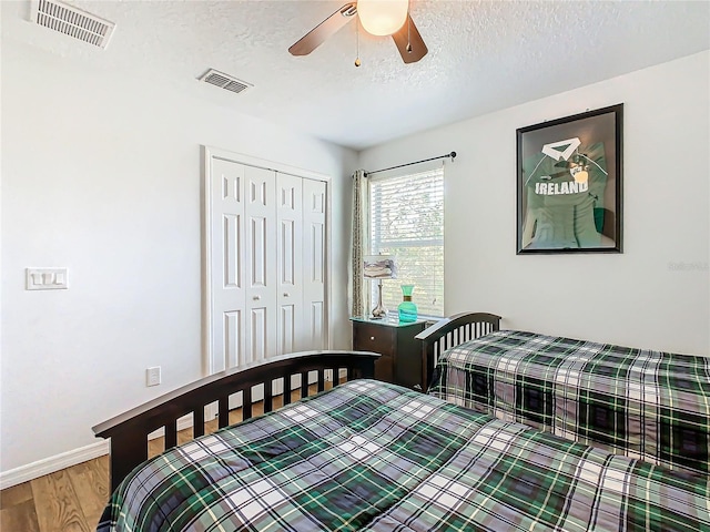 bedroom featuring a textured ceiling, a closet, wood finished floors, and visible vents