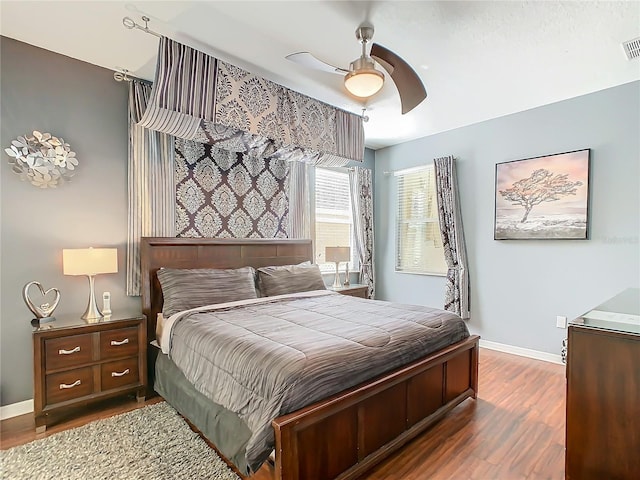 bedroom with ceiling fan, wood finished floors, visible vents, and baseboards