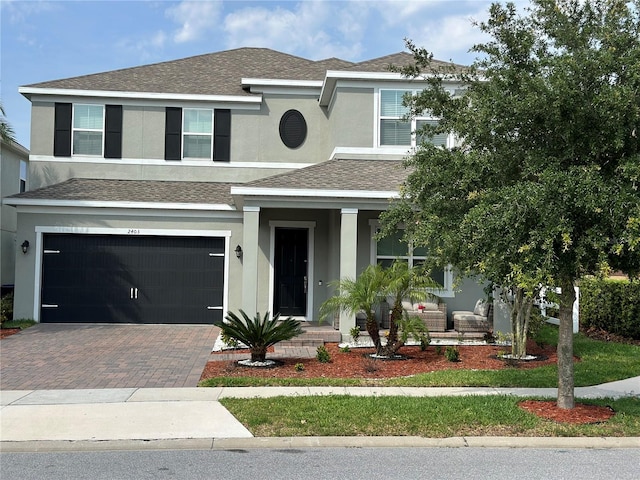 view of front of house featuring a porch, an attached garage, a shingled roof, decorative driveway, and stucco siding