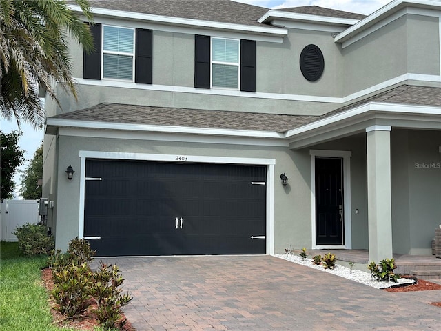 view of front facade with an attached garage, a shingled roof, fence, decorative driveway, and stucco siding