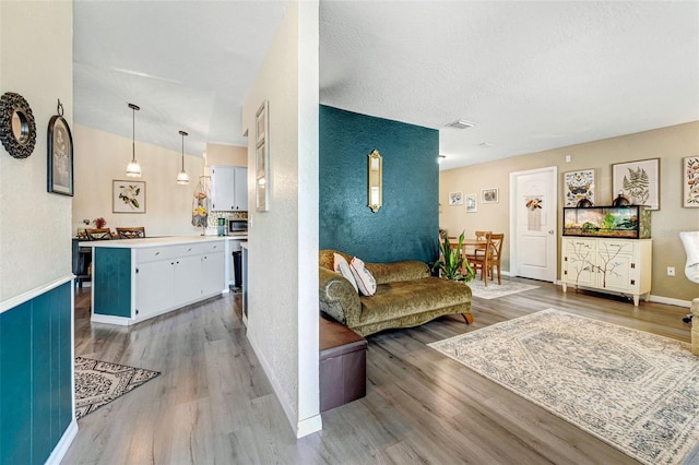 living area featuring visible vents, a textured ceiling, baseboards, and wood finished floors