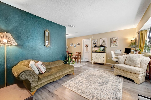 living room featuring a textured ceiling, an accent wall, baseboards, and wood finished floors