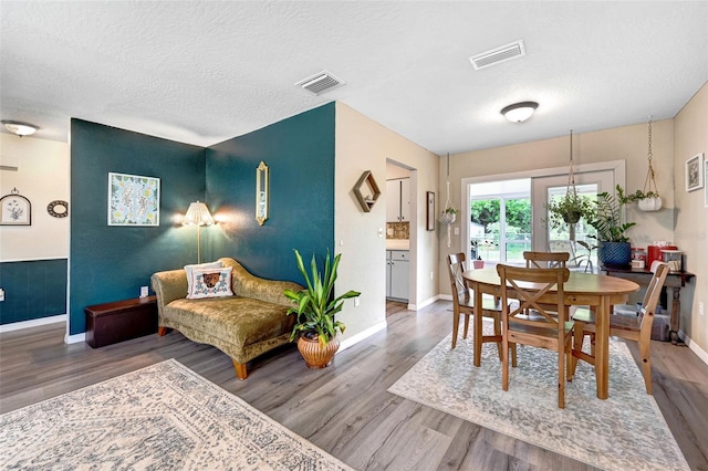 dining space with visible vents, a textured ceiling, and wood finished floors