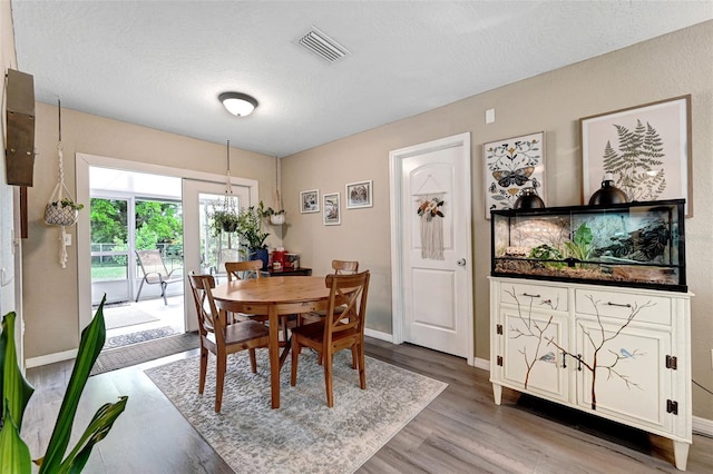 dining room with light wood finished floors, baseboards, visible vents, and a textured ceiling