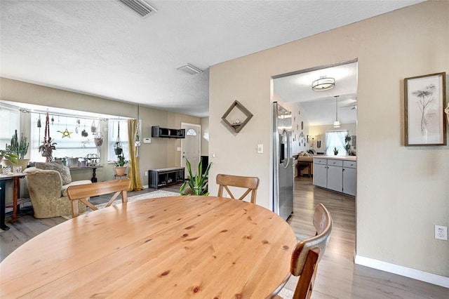 dining room featuring a textured ceiling, wood finished floors, visible vents, and baseboards