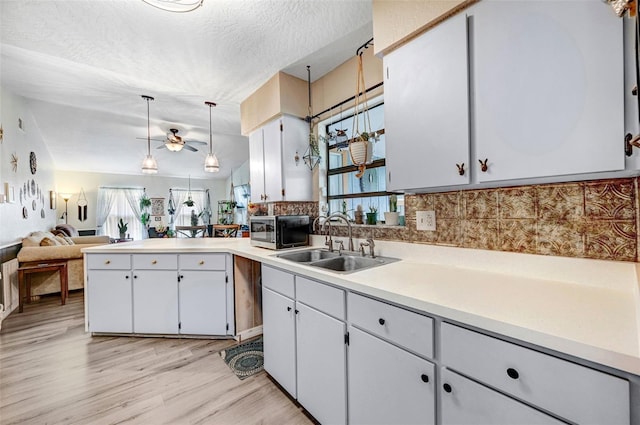 kitchen featuring a peninsula, a sink, light countertops, light wood finished floors, and stainless steel microwave