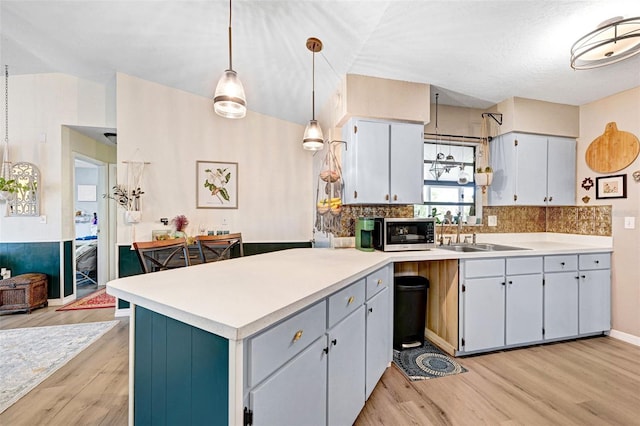 kitchen featuring light countertops, stainless steel microwave, light wood-style flooring, a sink, and a peninsula