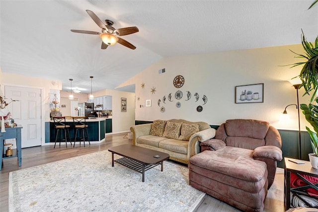 living area featuring vaulted ceiling, ceiling fan, light wood-type flooring, and visible vents