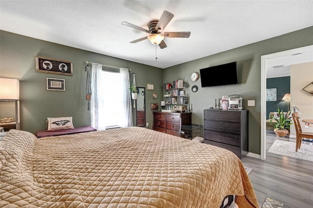 bedroom featuring a textured ceiling, a textured wall, ceiling fan, wood finished floors, and baseboards