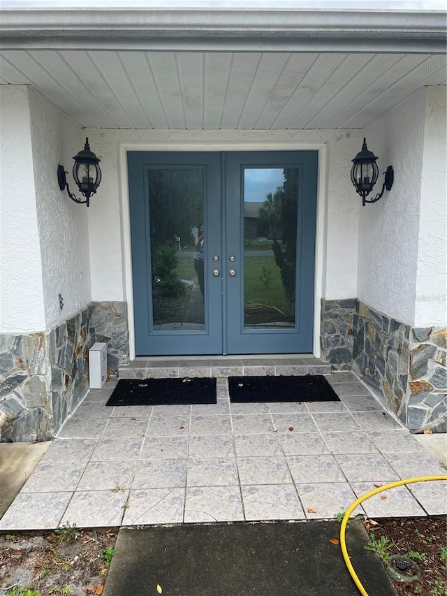 entrance to property with stone siding, french doors, and stucco siding