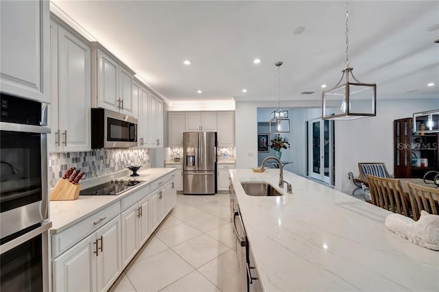 kitchen with light tile patterned floors, tasteful backsplash, appliances with stainless steel finishes, light stone countertops, and a sink