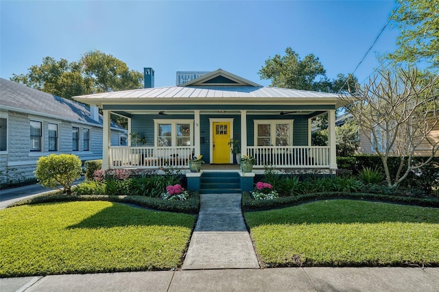 bungalow featuring covered porch, metal roof, a front lawn, and ceiling fan