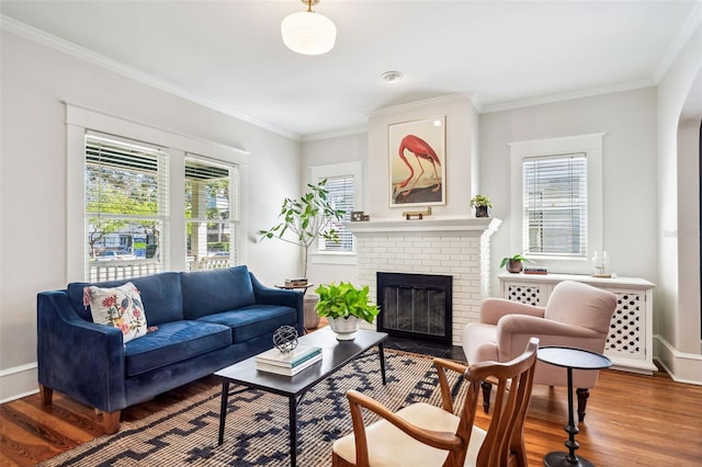 living room with a brick fireplace, wood finished floors, baseboards, and ornamental molding