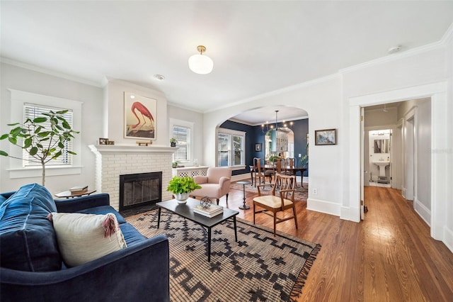 living area with baseboards, arched walkways, wood finished floors, and crown molding