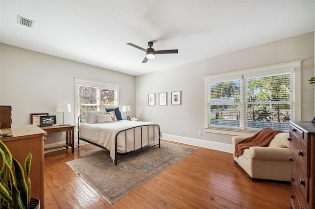 bedroom with a ceiling fan, visible vents, baseboards, and wood-type flooring