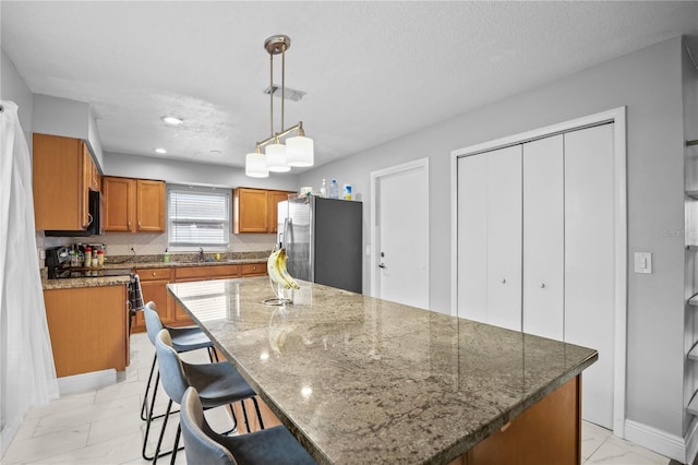 kitchen featuring visible vents, marble finish floor, freestanding refrigerator, a center island, and brown cabinetry