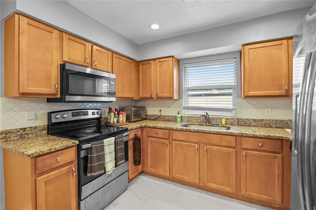 kitchen with light stone counters, stainless steel appliances, a sink, marble finish floor, and decorative backsplash