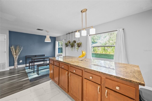 kitchen featuring visible vents, brown cabinets, light stone countertops, marble finish floor, and pendant lighting