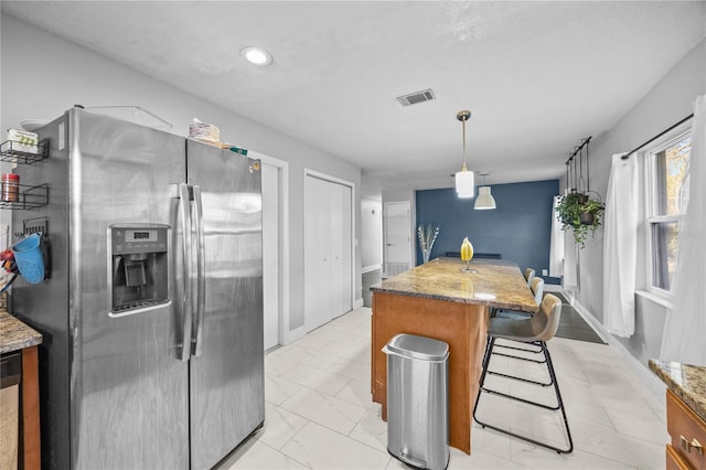 kitchen featuring marble finish floor, stainless steel refrigerator with ice dispenser, visible vents, a kitchen island, and light stone countertops