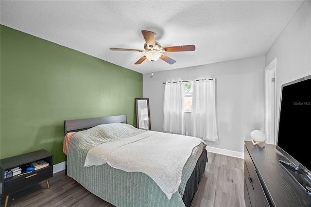 bedroom with a ceiling fan, a textured ceiling, baseboards, and wood finished floors