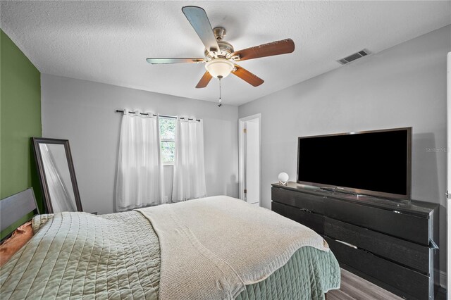 bedroom with a ceiling fan, a textured ceiling, visible vents, and wood finished floors