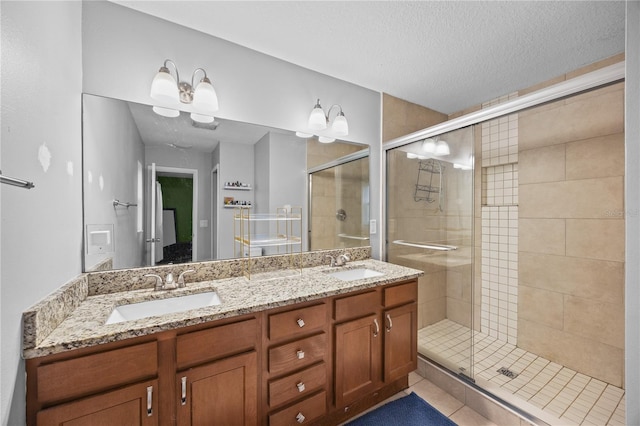 full bath featuring double vanity, a stall shower, a textured ceiling, and a sink