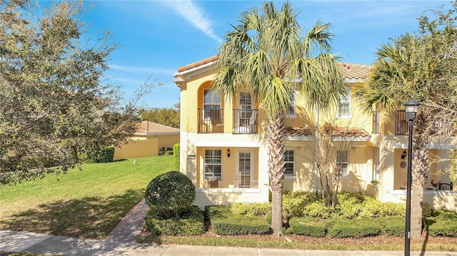 mediterranean / spanish home featuring a balcony, a tiled roof, a front lawn, and stucco siding