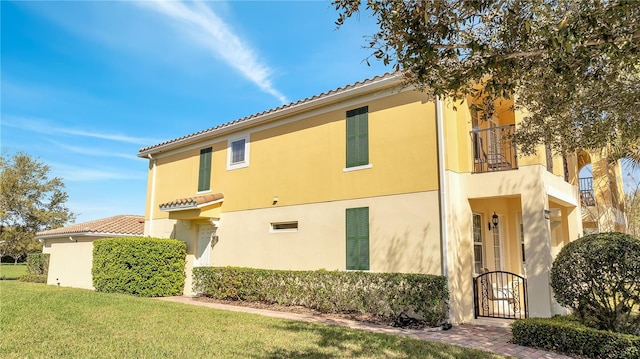 view of property exterior with a balcony, a gate, a lawn, and stucco siding