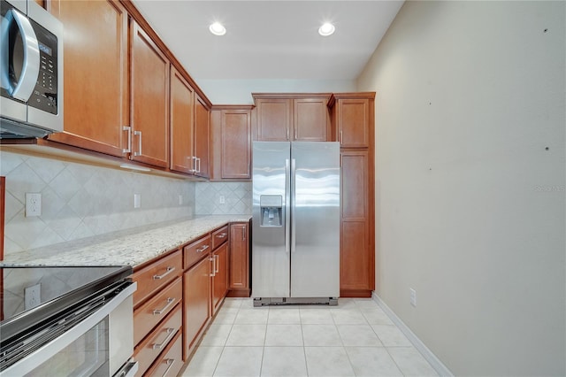 kitchen featuring light tile patterned floors, stainless steel appliances, backsplash, light stone countertops, and brown cabinetry